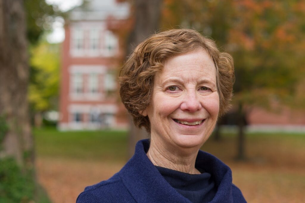 Headshot photo of Dr. Janet Polasky, and older women with short auburn hair curling just short of below her ears. She is wearing a navy blue sweater over a black straight neckline shirt. She looks very kind.